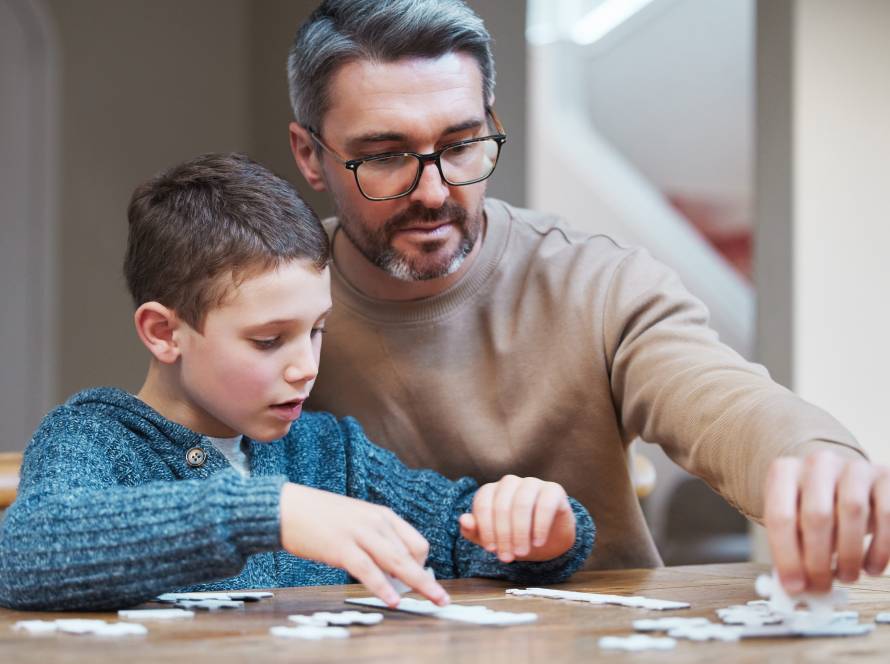 Adult and child assembling jigsaw puzzle together at wooden table during supportive interaction